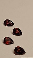 Four pear cut garnet gemstones arranged on neutral background showing color and cut