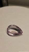 Pink amethyst pear cut gemstone on a plain white surface, showing the faceted cut and clarity.