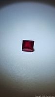 Close-up photo of a square cut ruby gemstone showing deep blood red color under focused light.