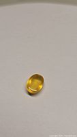 Oval cabochon cut yellow opal gemstone with smooth polished surface on plain background.