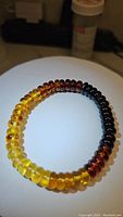 Photo of chunky Baltic amber bracelet showing gradient color from light yellow to black beads, laid on a white surface with a pill bottle in background