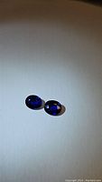 Pair of deep royal blue oval cut natural Ceylon sapphires on a light background showing rich color and clarity.