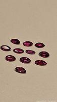 Twelve natural, untreated marquis cut rubies, deep exotic fuchsia hot pink to red color, showing clarity and shine, laid out on a plain surface under bright light.