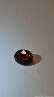 Oval faceted red gemstone on white textured surface
