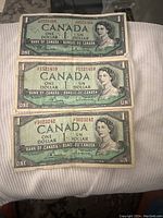 Three 1954 Canadian one dollar bills front side showing Queen Elizabeth II portraits and serial numbers.