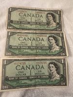 Front side of three 1954 Canadian 1 dollar bills showing Queen Elizabeth II portraits and serial numbers.