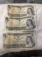Photo of three 1973 Canadian one dollar bills front side showing Queen Elizabeth II and bank details, serial numbers visible.