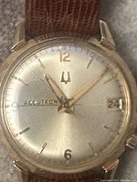 Close-up of watch face showing Accutron dial, date window at 3 and tuning fork logo, gold-tone case and sunburst silver dial