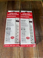 Two boxed new power strips with red and white packaging, showing front with product name and features.
