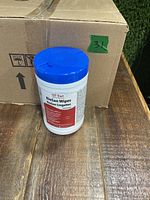 Single container of QT-San BioSan Wipes with blue cap placed in front of a cardboard box.