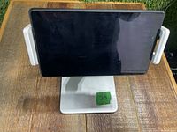 Front view showing a tablet held between two white padded grips on a silver stand.