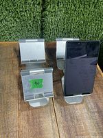 Four silver-colored aluminum tablet stands positioned on wooden surface, one holding a small black tablet.
