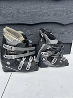 Two pairs of ski boots side by side showing full buckles and straps on the exterior, black and gray color