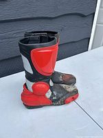 Side angle showing red and gray molded protective shin and heel areas on the black boots with visible dirt and wear