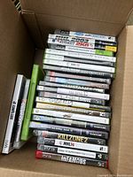 Photo of a box filled with 22 video game cases from multiple consoles including Xbox 360, PlayStation 3, PlayStation 2, Wii, and PSP.