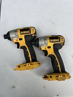 Two Dewalt cordless impact drills placed side-by-side lying on a flat surface. Both drills are missing batteries and show signs of use.