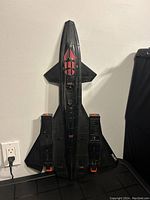 Black GI Joe vintage toy fighter jet with orange accents and visible cockpit, resting upright against a wall.