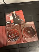 Opened red game case showing two PS3 game discs and accompanying manuals and pamphlets laid flat for display.