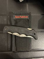 Black Kershaw folding pocket knife with serrated blade resting on black Kershaw branded nylon sheath.