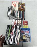 Photo of mixed media lot including DVDs, one Blu-Ray disc, VHS tapes, cassette tapes, and CDs arranged on a table.