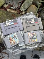 Photo of four vintage video game cartridges for Super Nintendo and Nintendo 64. Shows two SNES cartridges NHL 94 and John Madden Football, and two N64 cartridges Madden 99 and NFL Quarterback Club 99, all in used condition with visible labels.