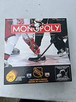Front cover of NHL Monopoly Collector's Edition board game box showing hockey players' legs, sticks, NHL logos, and collectible tokens information.