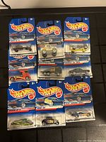Nine sealed Hot Wheels toy cars laid out and photographed on a flat black surface, showing front side of packaging with models and designs visible.