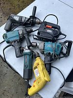 Photo showing six electric power tools: two Makita drills, one Black & Decker jigsaw, one Mastercraft drill, one Craftsman drill, and one Black & Decker drill. All plugged-in corded models with visible wear.