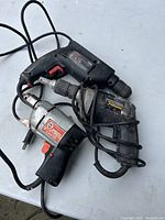 Three variable speed electric drills tangled with cords on a surface. Drills show signs of use and wear.