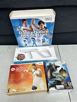 Photo showing three boxed Nintendo Wii games: Dance Dance Revolution with dance mat controller box, Active Life game, and Monster Hunter Tri game.