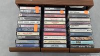 Cassette tapes stacked in three columns inside a drawer, visible tape packaging with titles and artists.
