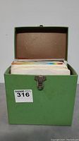 Green metal box containing a large quantity of 45 RPM vinyl records in paper sleeves.