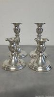 Four pewter candlestick holders, two smaller and two taller, shown together on gray surface.
