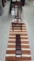 Full lot image showing vintage wooden chair placed on striped rug with shelving unit on the rug in foreground