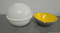 Two bowls shown: one white plastic dome-shaped container bowl and one decorative bowl with yellow interior and grey exterior with a notch on the rim.