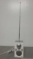 Front view of Tivoli Audio iPAL radio showing white faceplate, tuning dial, knobs, speaker grille, and extended antenna.