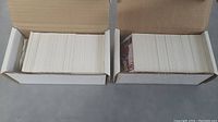 Two open white boxes filled with large quantity of unorganized hockey cards stacked vertically.