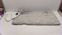 Gray quilted electrical heating pad laid out flat on a white surface showing soft fabric texture and rectangular shape.