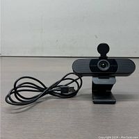 Front view of eMeet C960 webcam showing lens, privacy cover flipped open, USB cable coiled to side.