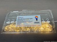 Packed 300 LED fairy curtain lights in clear plastic packaging with visible warm white LED lights and product label.