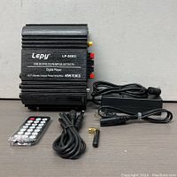 Front view of Lepy LP-269S amplifier with accessories including power adapter, remote control, audio cable, and antenna displayed on a table.