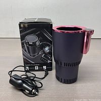 Full view of the black and rose gold auto cup holder with cable and box shown in the background on a wooden surface