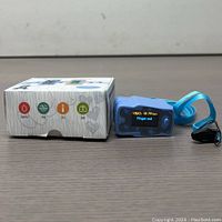 Volueth Pulse Oximeter with original box and lanyard on a wooden surface.