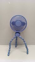 Front view of the light blue wireless mini fan mounted on flexible segmented tripod legs, showing the fan blades through the grill.
