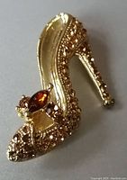 Front view of gold-tone high heel princess slipper brooch with amber Swarovski crystals and a larger marquise-shaped crystal near the toe.