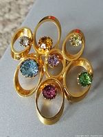 Front view of vintage gold tone brooch with seven multi-colored rhinestones set in open oval loops.