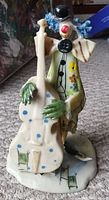 Front view of the colorful hand-painted porcelain clown figurine holding a stringed instrument, with details visible on the face, clothing, and instrument.