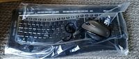 Microsoft wireless keyboard and mouse wrapped in plastic bag on carpeted floor