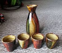 Full set view showing four cups and one sake bottle with multicolored glaze on carpeted floor.