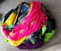 Top view of pile of 6 colorful scarves showing pink scarf with gold stars, yellow scarf, and dark colored scarves underneath